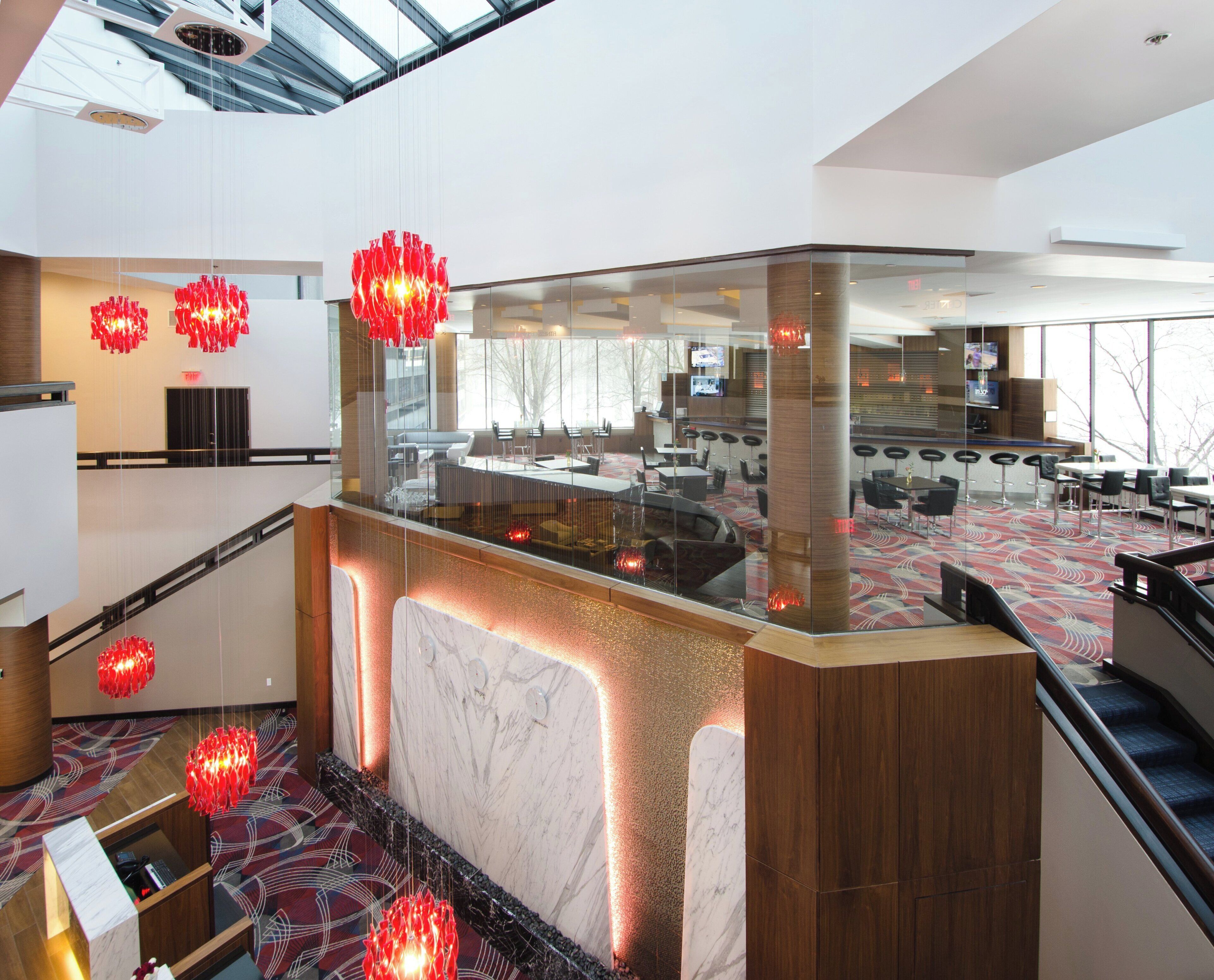 A modern hotel lobby with a glass partition, seating areas, and a patterned carpet.