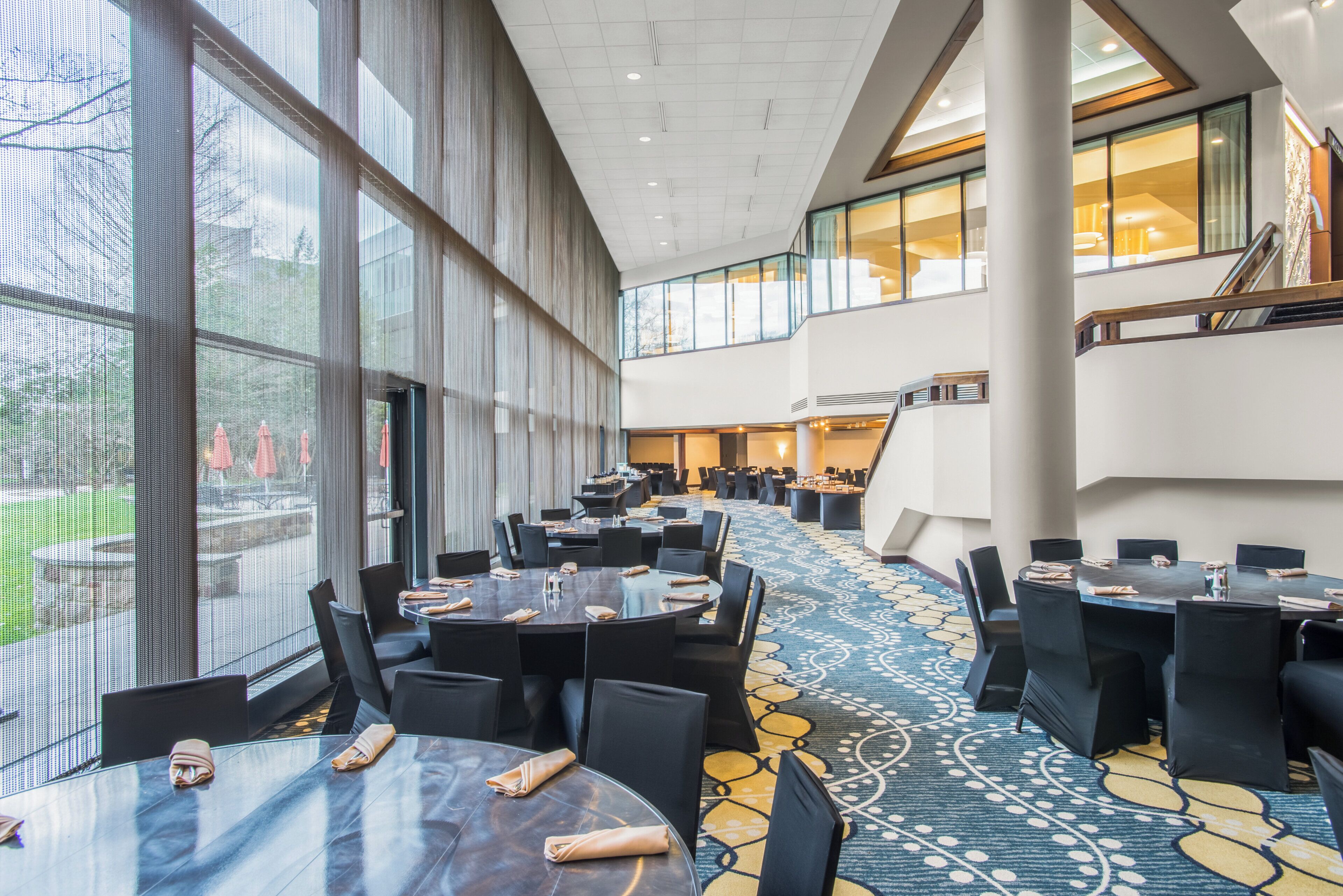 A hotel lobby with multiple dining tables, chairs, and a large window overlooking a garden.