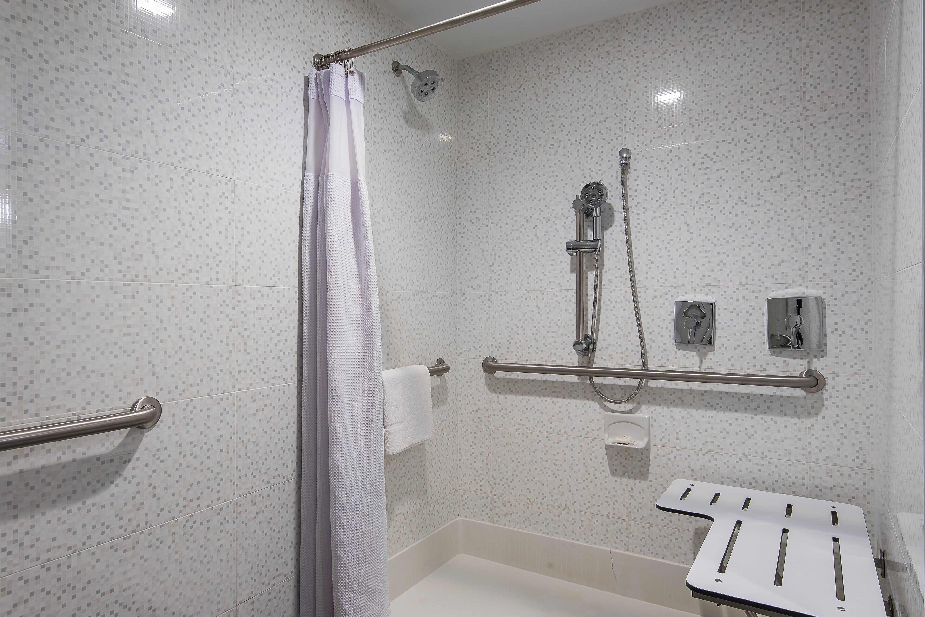 A bathroom with a shower, grab bars, a toilet, and a hand dryer.