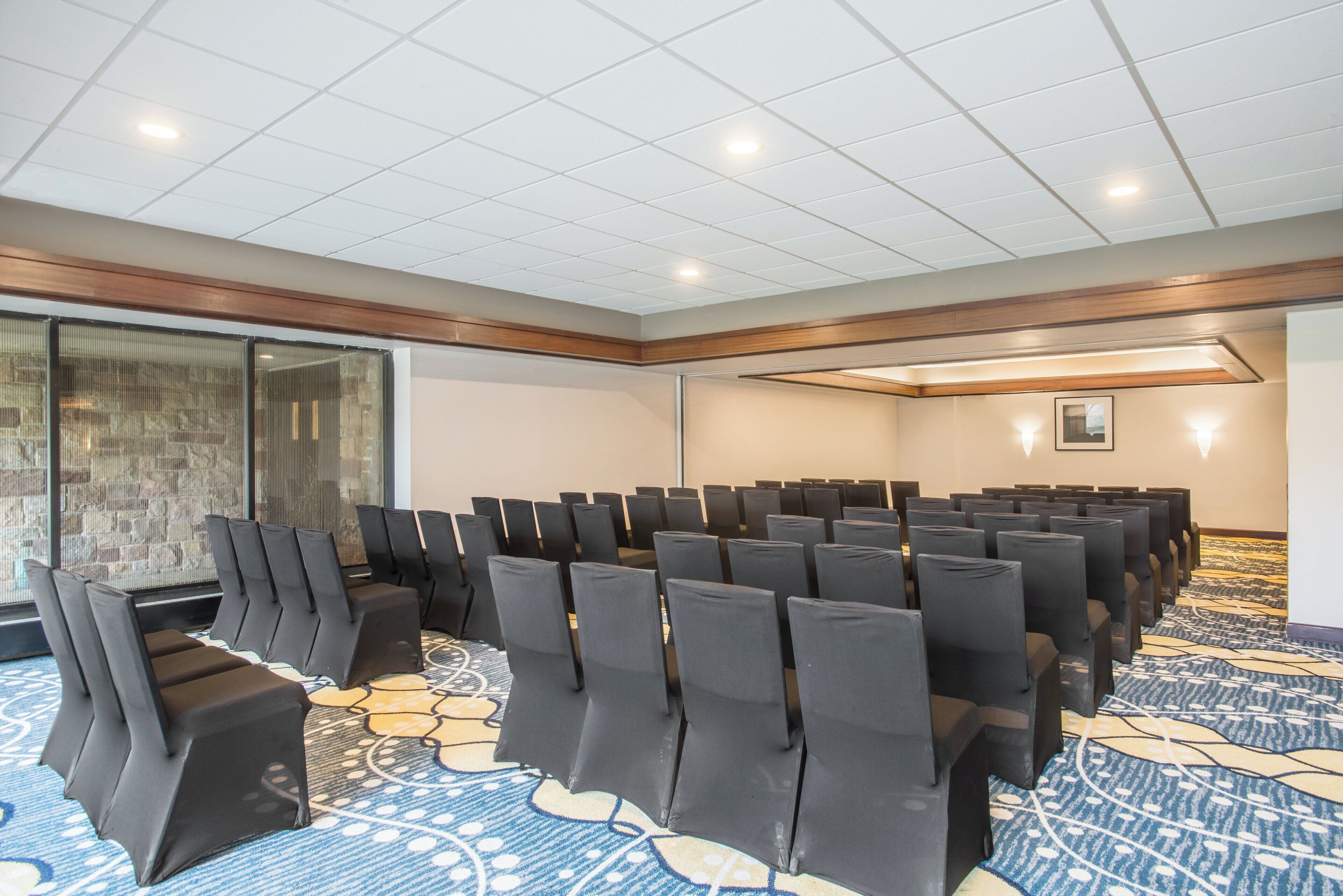 A conference room with rows of black chairs, a patterned carpet, and a stone wall with windows.