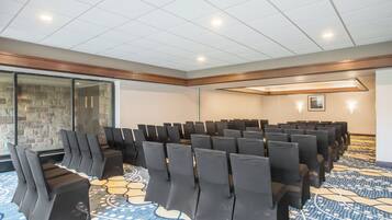 A conference room with rows of black chairs, a patterned carpet, and a stone wall with windows.