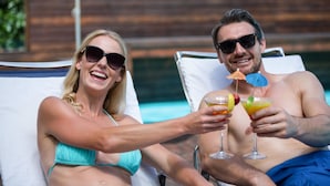 Two people reclining on sun loungers by a pool, holding drinks.