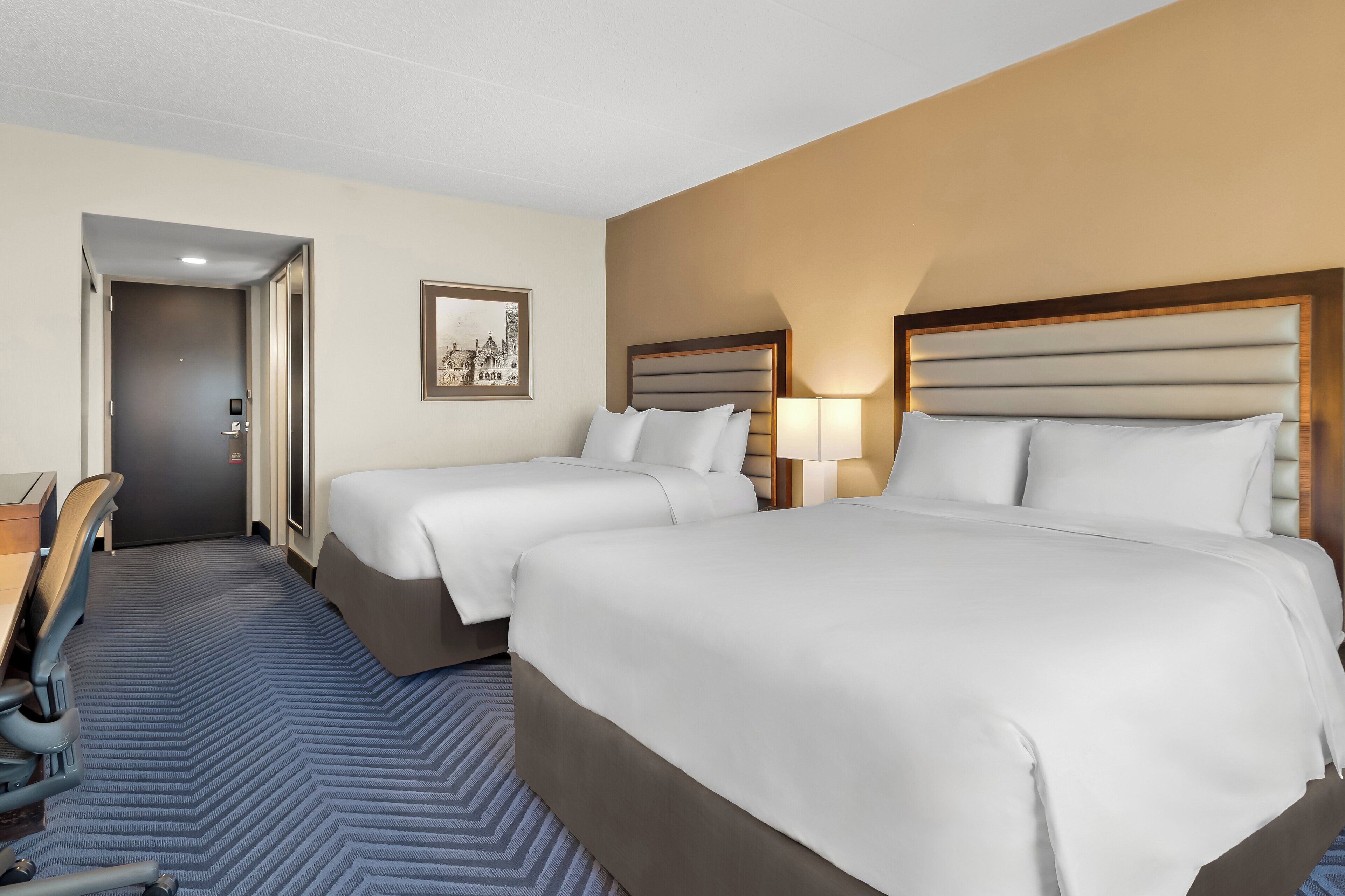 A hotel room with two beds, a desk, and a chair.