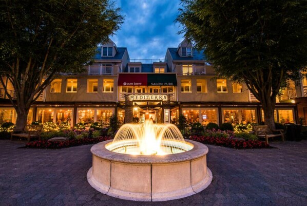 A hotel with a central fountain, multiple storefronts, and a well-lit facade.