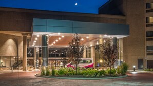 A hotel entrance with a covered waiting area, a bus stop, and a landscaped garden.