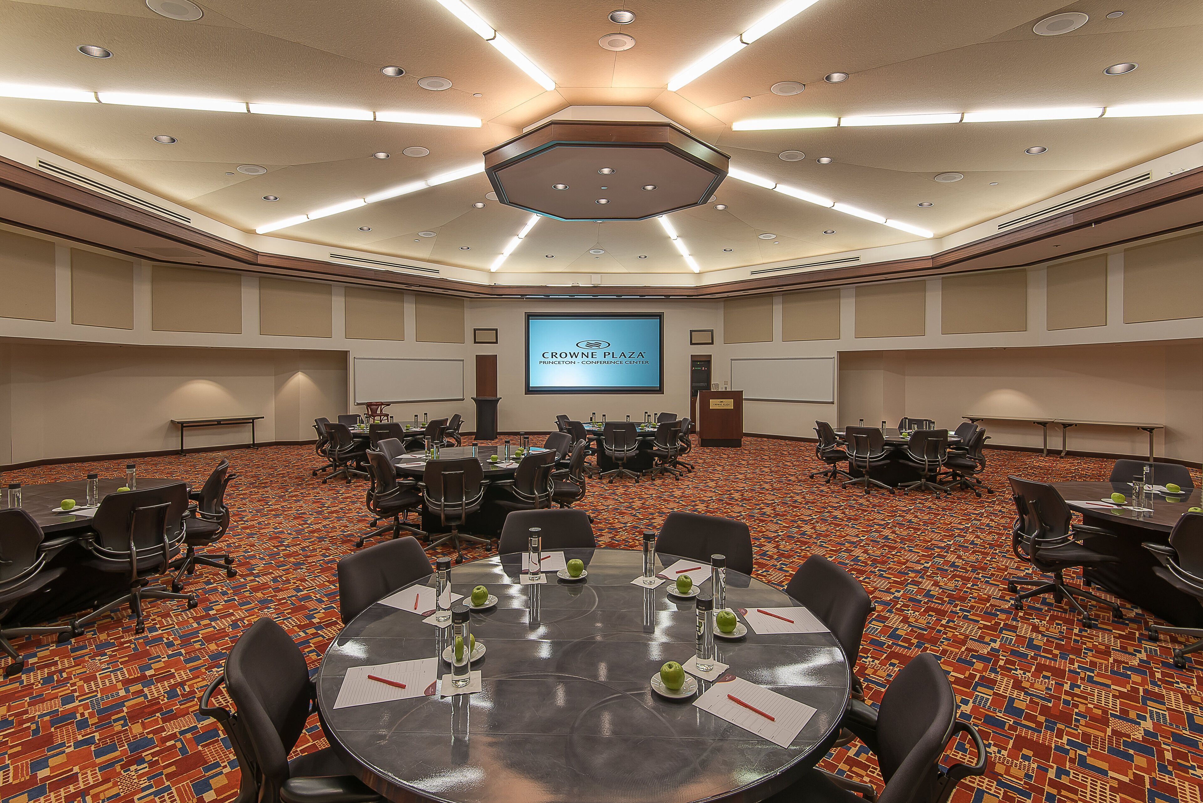 A conference room with round tables, chairs, and a large screen displaying "CROWNE PLAZA".