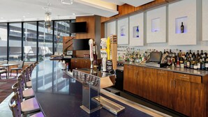 A modern bar area with a long counter, bar stools, and a variety of liquor bottles.