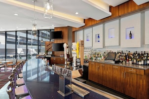 Un área de bar moderna con una barra larga, taburetes y una variedad de botellas de licor.