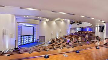 A modern auditorium with tiered seating, a stage, and a large screen.