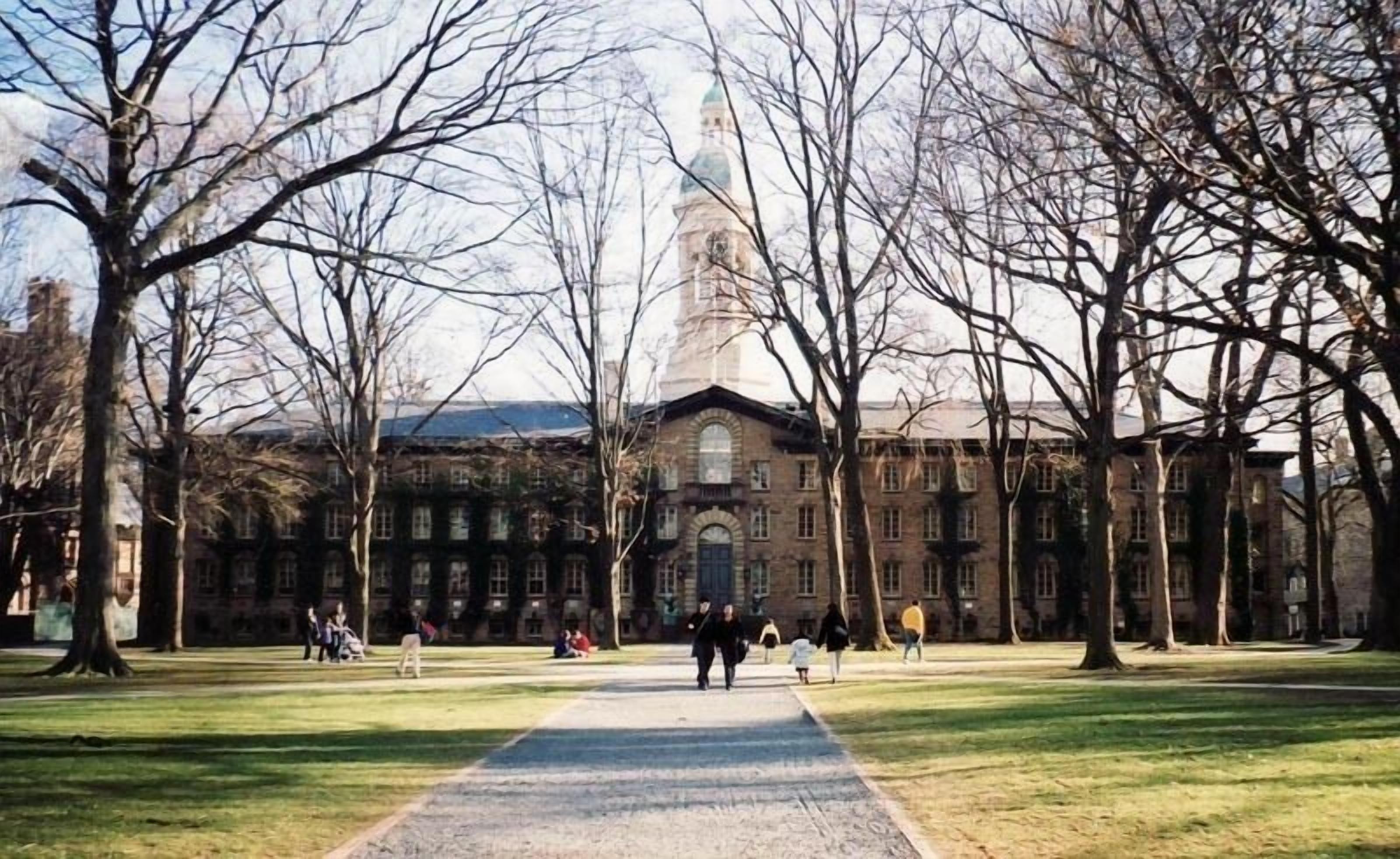 A pathway leading to a historic building with a prominent tower, surrounded by trees and a grassy area.