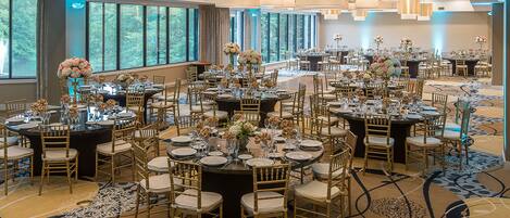 Un amplio salón de banquetes con mesas redondas, sillas doradas y centros de mesa florales.