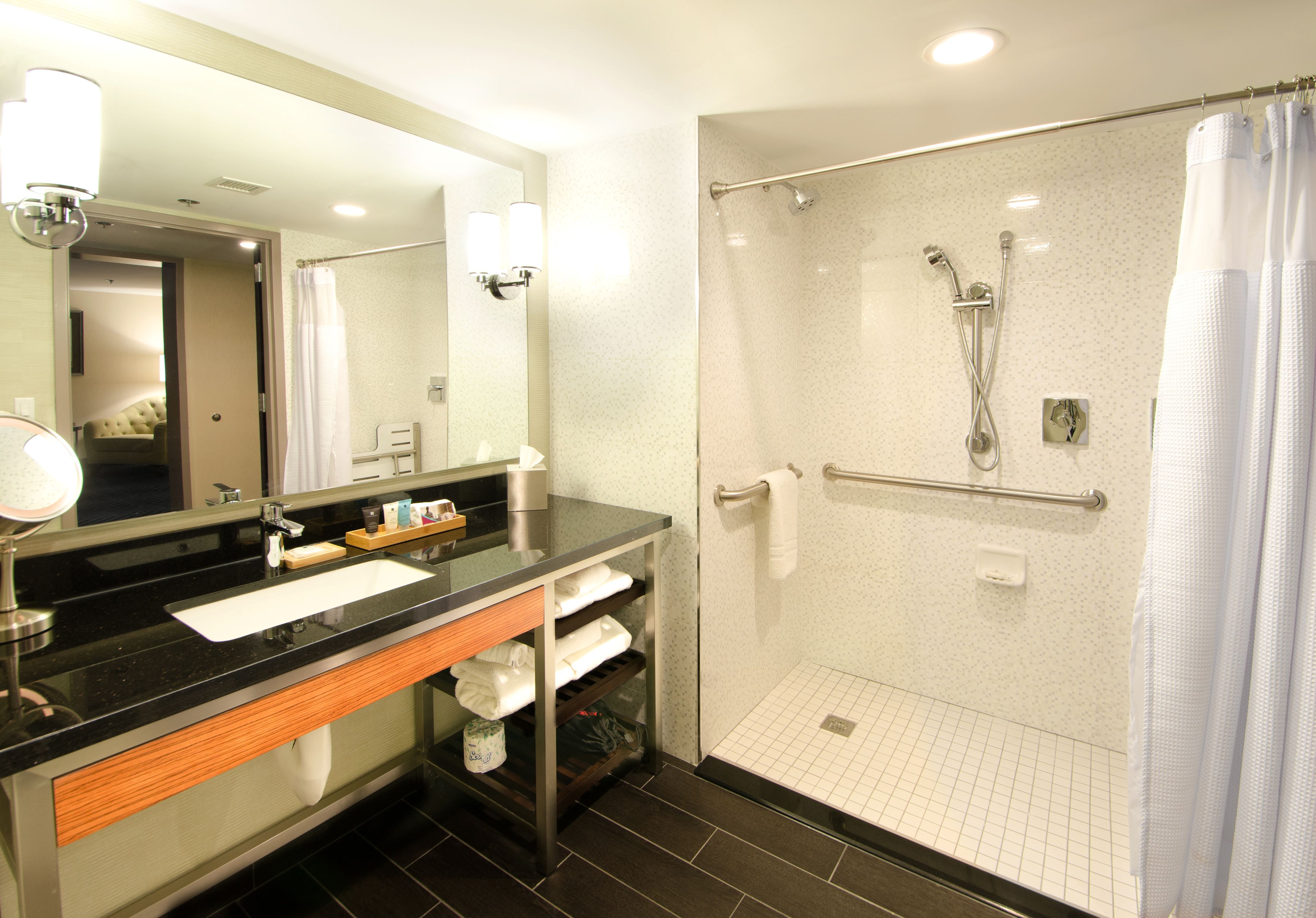 Un baño moderno con un mostrador negro, ducha con mampara de vidrio y espejo con iluminación.