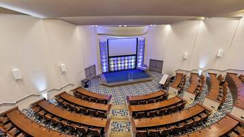 Ein großes Auditorium mit abgestuften Sitzreihen und einer zentralen Bühne.