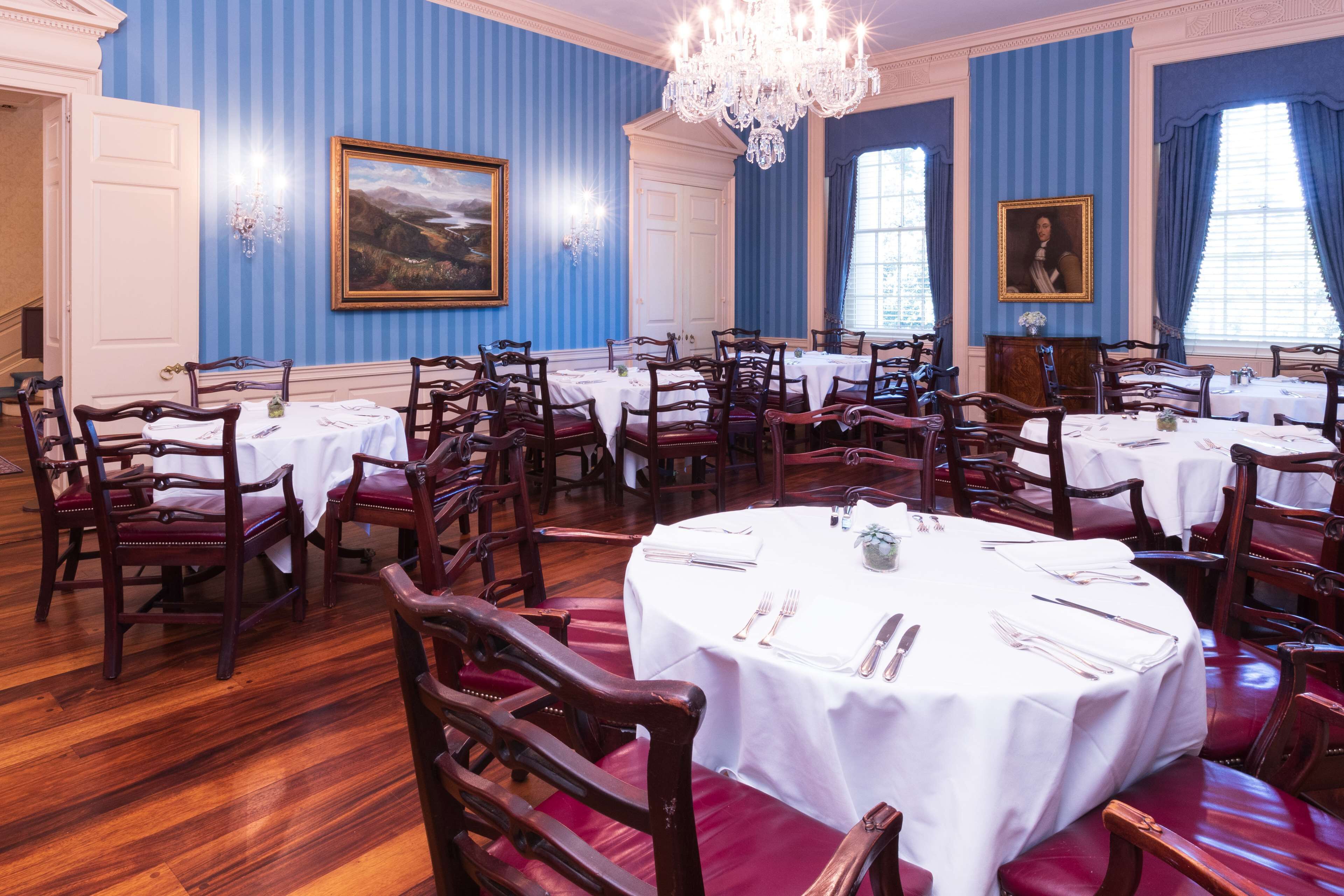 A formal dining room with multiple round tables set for service, wooden chairs, and a chandelier.