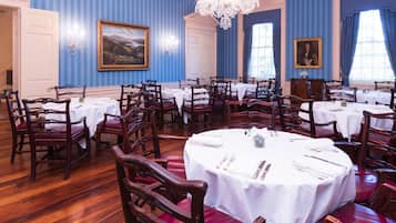 A formal dining room with multiple round tables set for service, wooden chairs, and a chandelier.