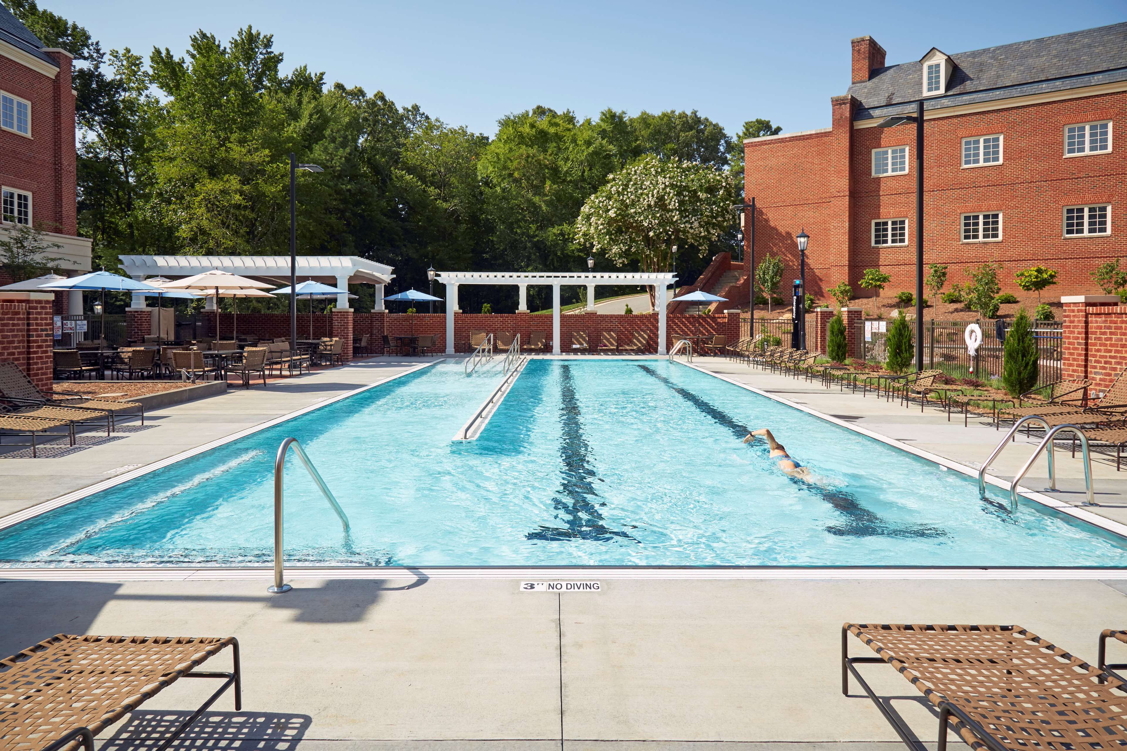 A swimming pool with lounge chairs and umbrellas, surrounded by brick buildings and trees.