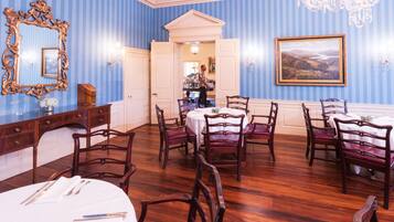 A dining room with striped blue walls, a chandelier, and a large mirror.