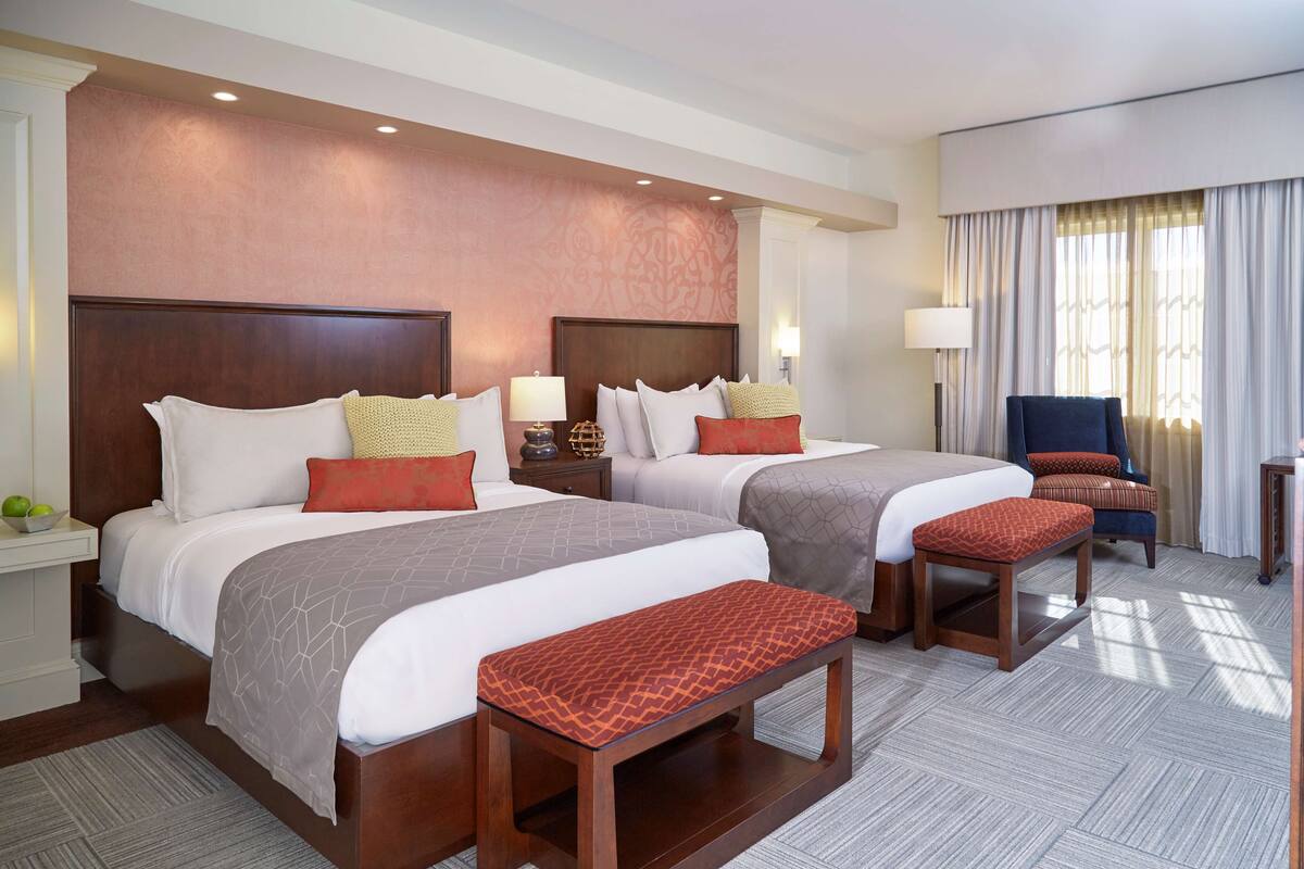 A hotel room with two beds, a bench, a chair, and a desk.