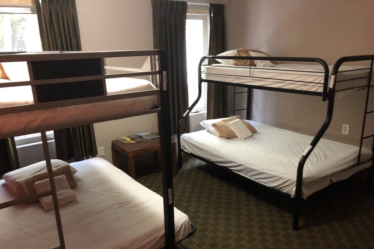 Une chambre avec un lit superposé, une table de chevet en bois et une fenêtre avec des rideaux.