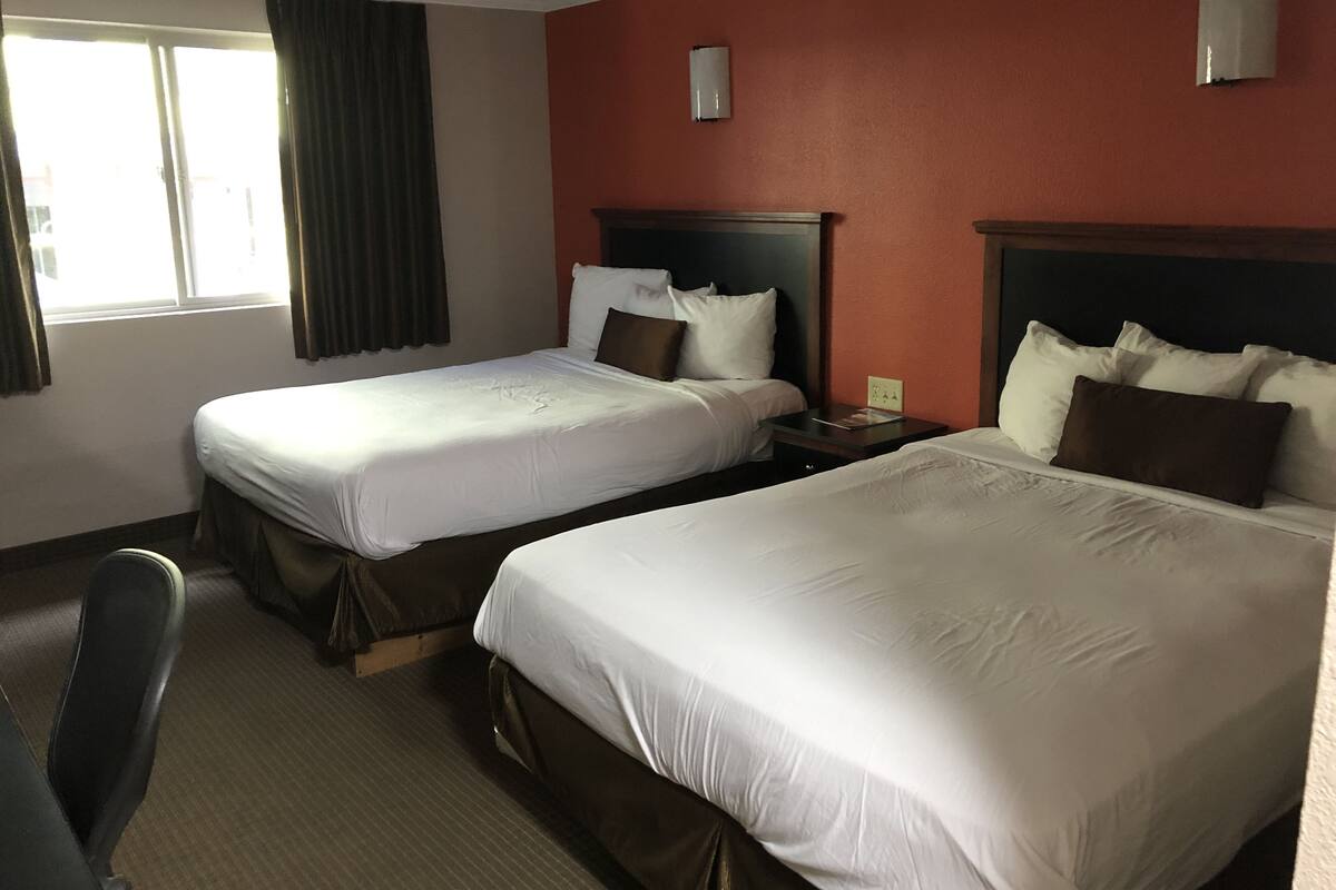 Une chambre d’hôtel avec deux lits, une table de chevet, une chaise et une fenêtre avec des rideaux.