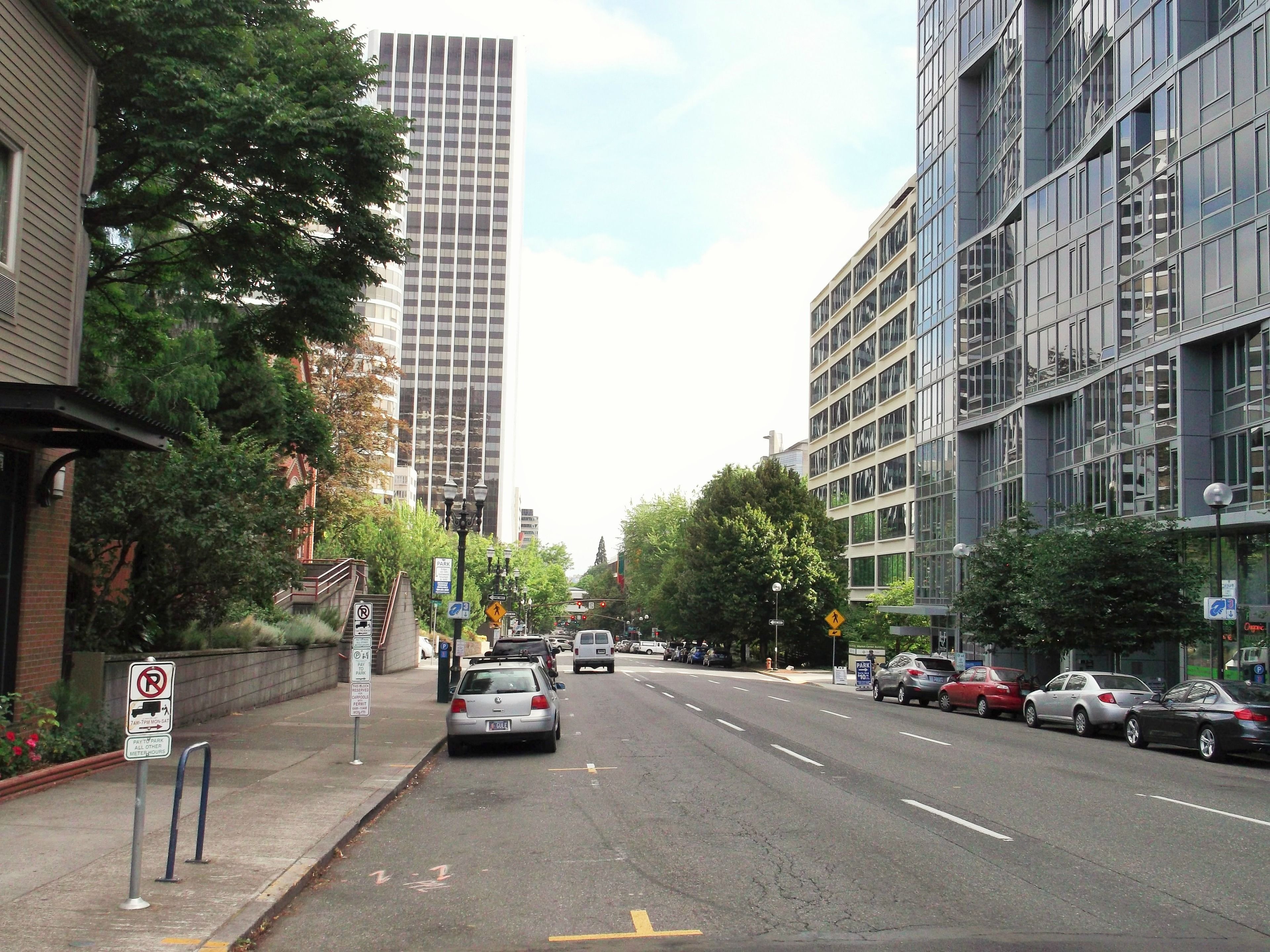 Una calle urbana con edificios modernos, coches estacionados y señales de tráfico.
