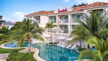 A hotel with a swimming pool surrounded by palm trees and lounge chairs.