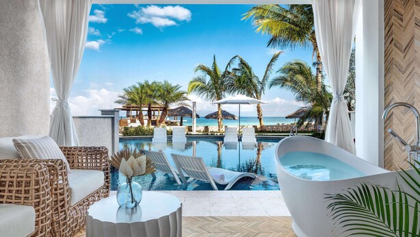 Ein luxuriöser Innenpoolbereich mit Meerblick, eine große Badewanne, Korbmöbel und ein Tisch mit einer Vase.