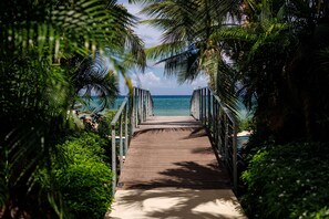 A wooden pathway leading to a beach, surrounded by lush greenery and palm trees.