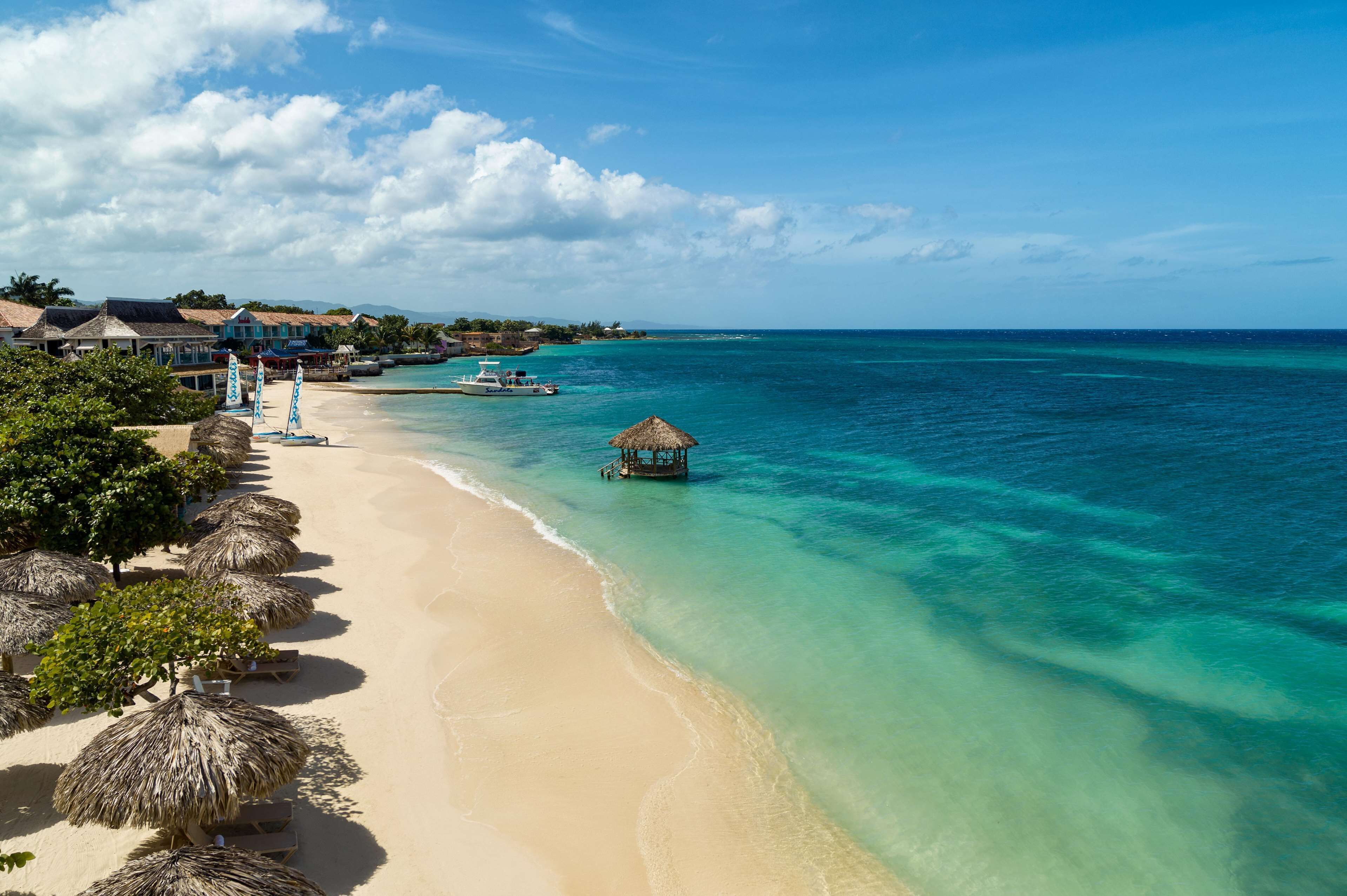A beach with clear turquoise water, a thatched hut, and a row of beach umbrellas.