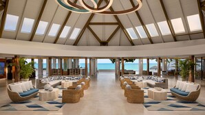 Un vestíbulo espacioso con mobiliario de mimbre, ventanas amplias y vista al mar.
