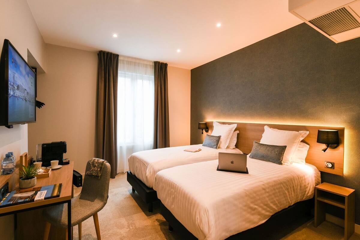 Habitación de hotel con dos camas, un escritorio con una computadora portátil, un televisor y una cafetera.