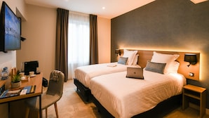 A hotel room with two beds, a desk with a laptop, a TV, and a chair.