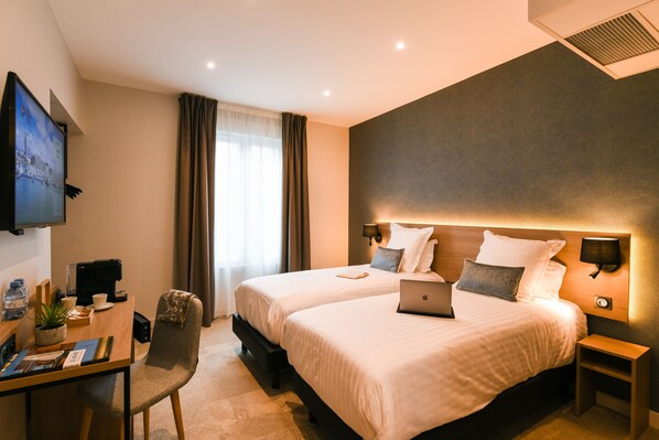 Une chambre d’hôtel avec deux lits, un bureau avec un ordinateur portable, une télévision et une chaise.