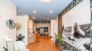 A hotel lobby with a wooden floor, a reception desk, a white chair, and a wall with a large ocean wave mural.