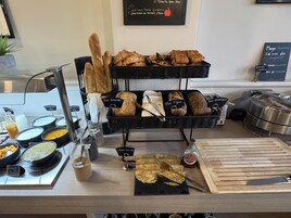 Una vitrina de panadería con panes y pasteles varios, una máquina de café y condimentos.