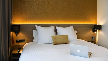 Una cama bien tendida con sábanas blancas, una laptop y una almohada de color mostaza.