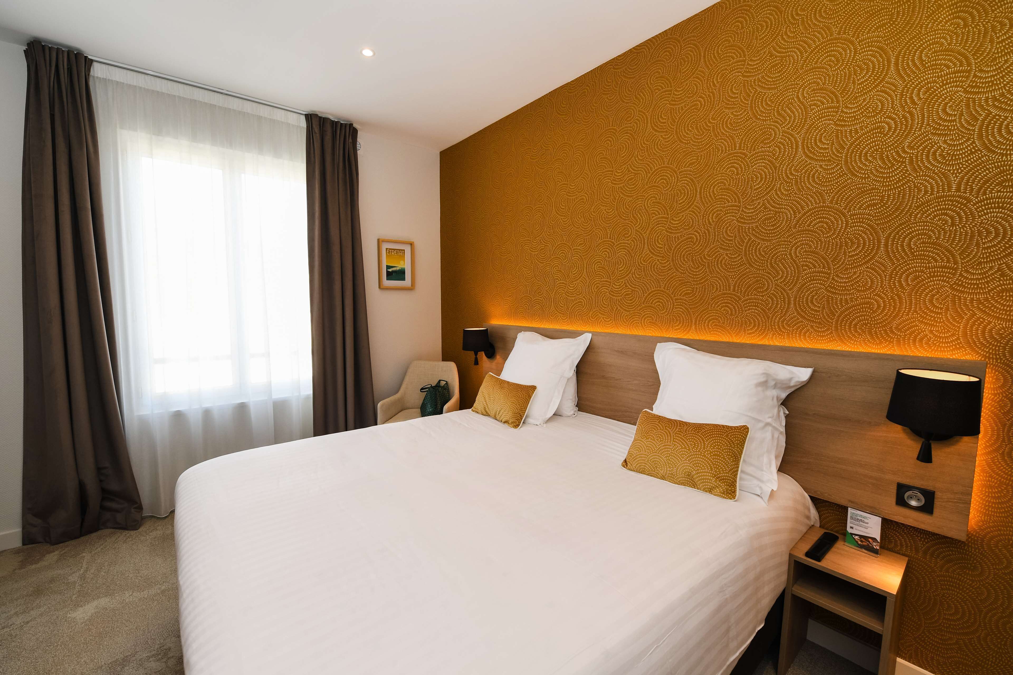 Una habitación de hotel con una cama grande, una mesita de noche, una lámpara y una silla.