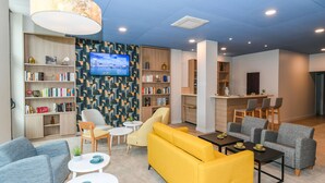 A modern hotel lobby with a seating area, bookshelves, a TV, and a bar.