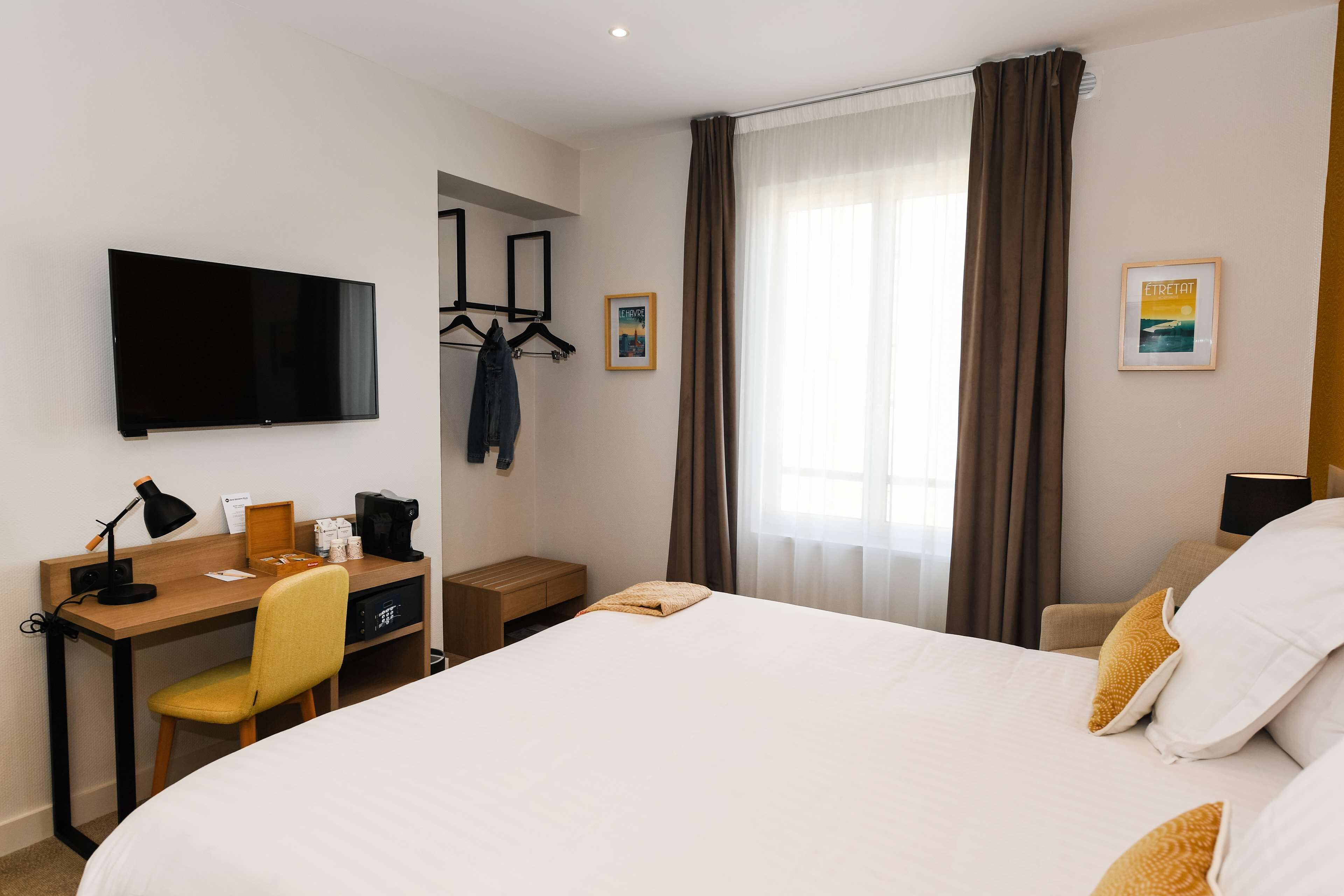 A hotel room with a bed, a desk with a chair, a TV, and a window with curtains.