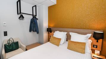 A hotel room with a bed, a chair, a hanging coat rack, and a wall with a patterned wallpaper.