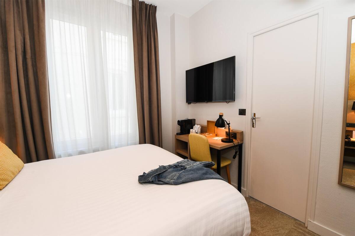 Una habitación de hotel con cama, escritorio, silla, televisión y puerta.