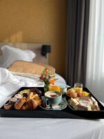 Una bandeja de desayuno con pasteles, una taza de café y un vaso de zumo de naranja sobre una cama con sábanas blancas y cabecero.