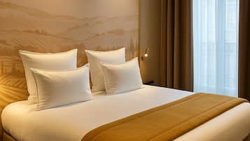 Una cama grande con ropa blanca y una manta marrón, un cabecero con una lámpara, y una ventana con cortinas translúcidas.