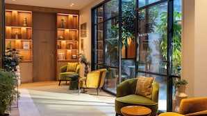 A modern interior with a large window, wooden shelving with decorative items, and comfortable seating. - Hotel Le Cardinal (Paris)