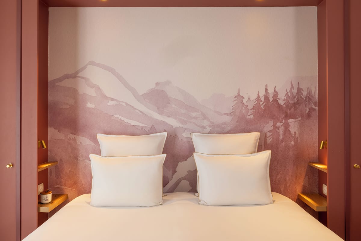 A bedroom with a mountain landscape mural, a bed with white linens, and two bedside tables with lamps.