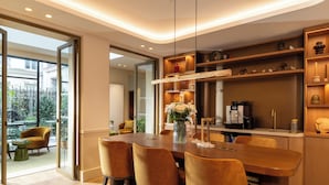 A modern kitchen with a wooden dining table, bar stools, and built-in shelves with kitchen appliances. - Hotel Le Cardinal (Paris)