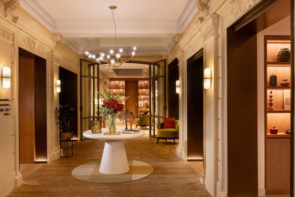 A hotel lobby with a central round table, a chandelier, and a reception desk. - Hotel Le Cardinal (Paris)