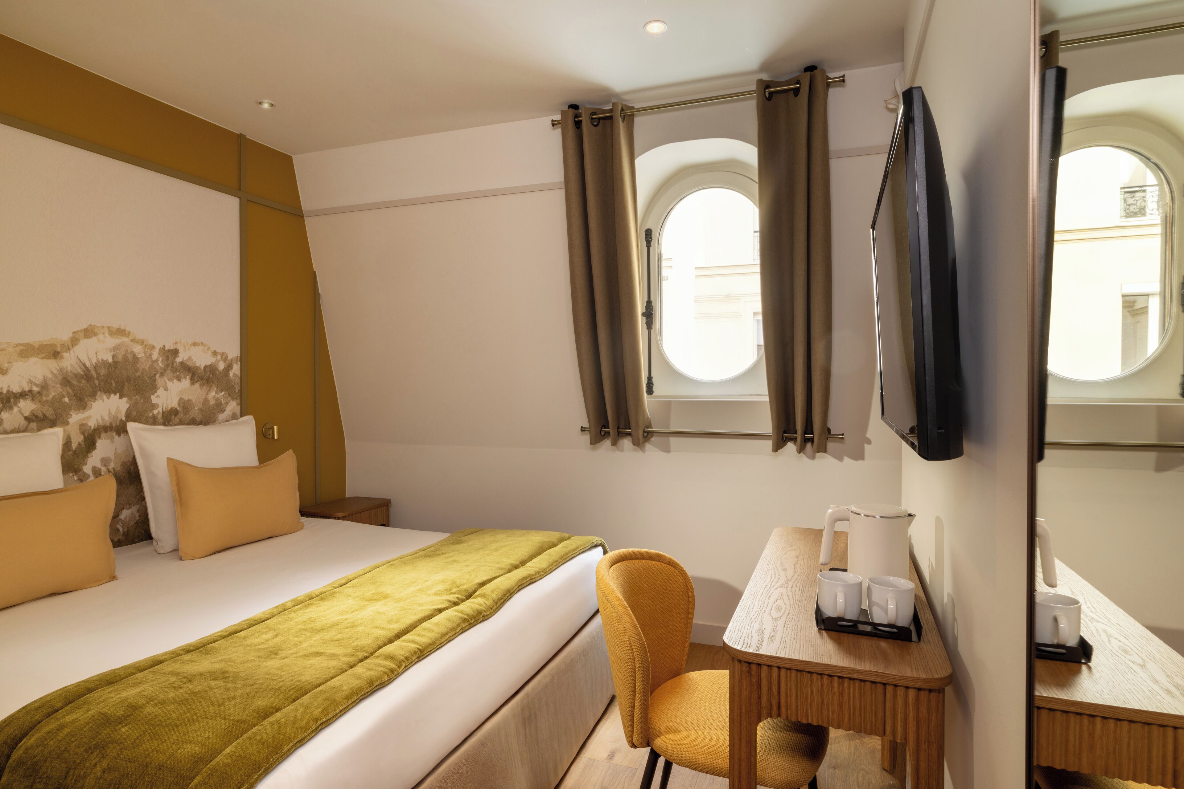Habitación de hotel con cama, escritorio con silla, ventana con cortinas y televisor de pantalla plana montado en la pared.
