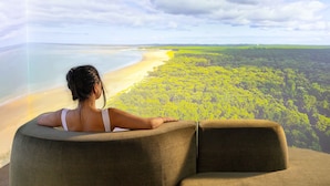 A person seated in a room with a view of a beach and forest. - Hotel Le Cardinal (Paris)