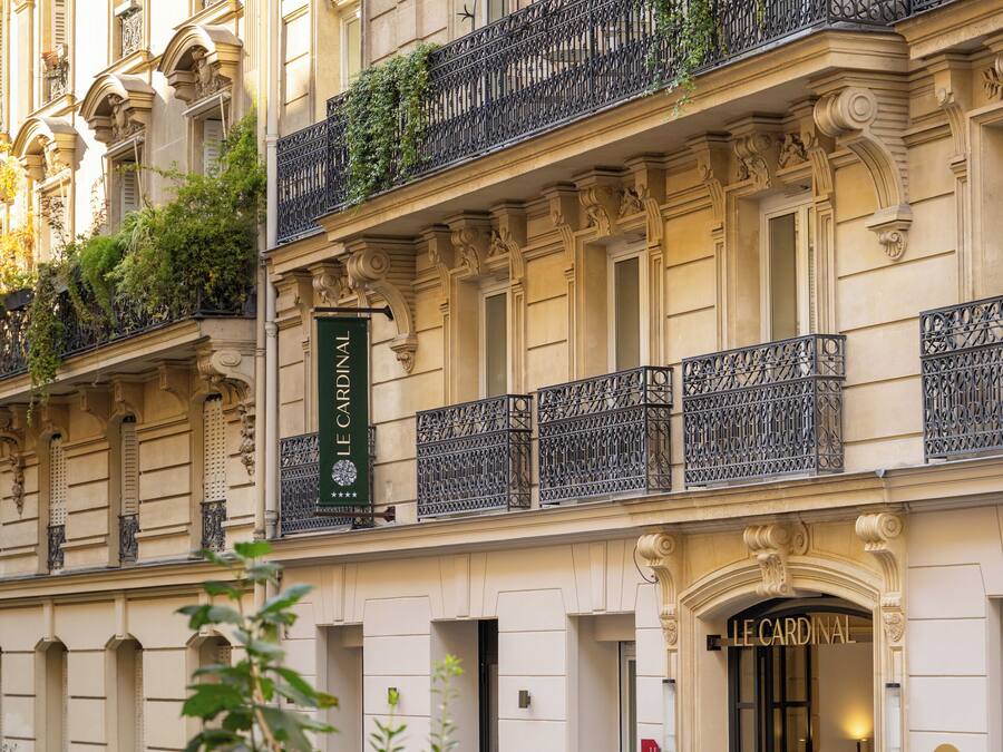 Un edificio con detalles arquitectónicos ornamentales, un cartel que dice "LE CARDINAL" y una entrada con rejas.